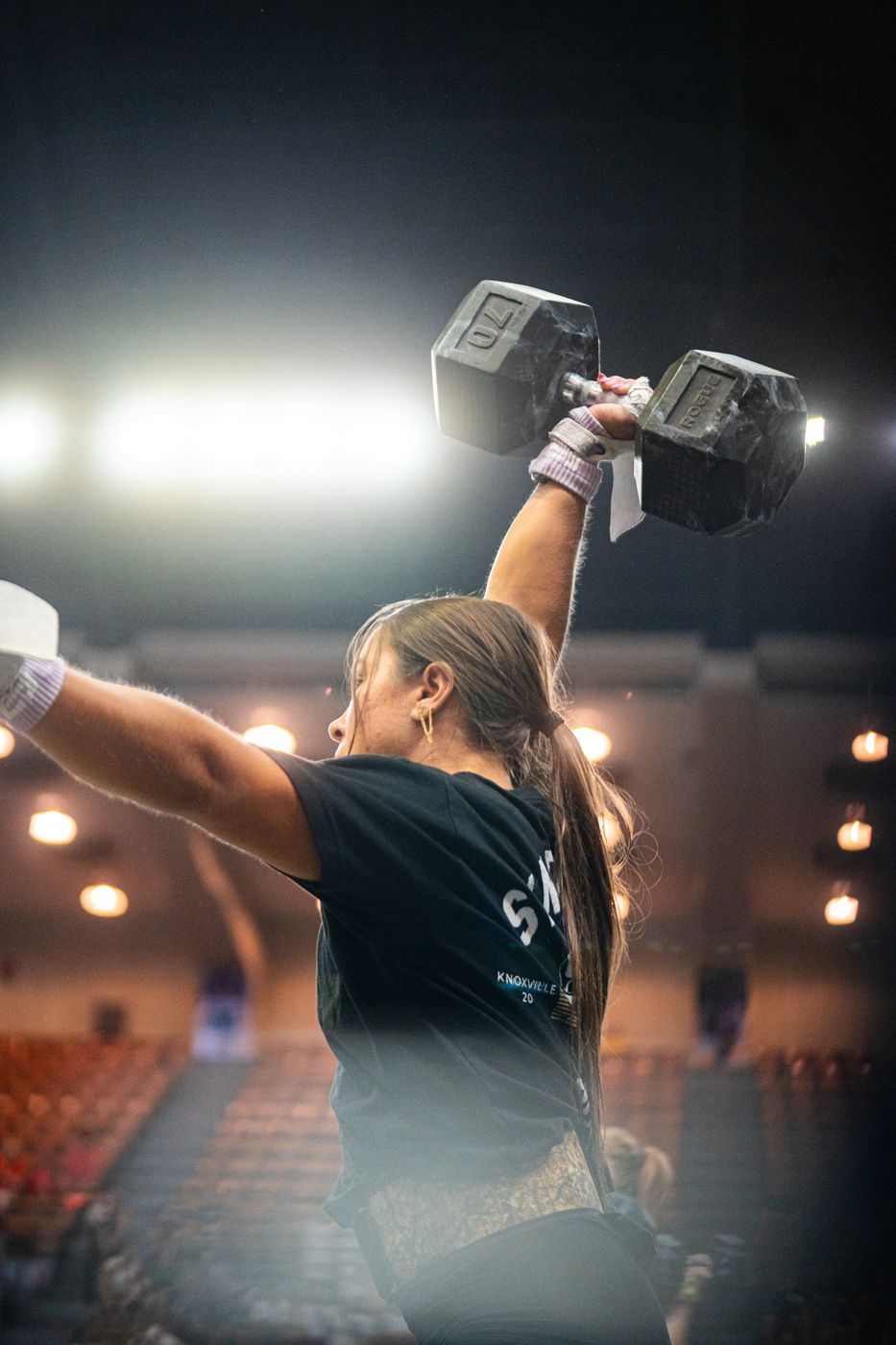 Dumbbell overhead under arena lights